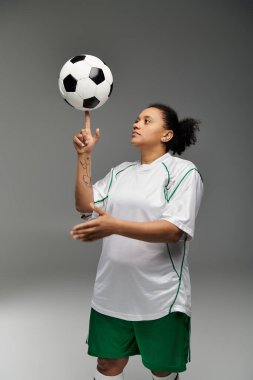 Beyaz formalı ve yeşil şortlu bir bayan sporcu parmak ucunda bir futbol topu çeviriyor..