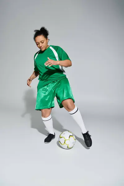 stock image A female athlete in a green jersey dribbles a soccer ball in a studio setting.