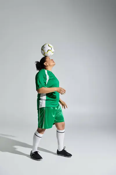 stock image A female athlete in a green jersey juggles a soccer ball on her head against a white background.