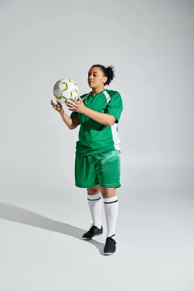 Stock image A female athlete in a green soccer jersey holds the ball before a game.