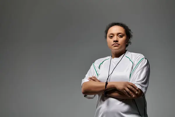 stock image A female athlete, wearing a white jersey with green accents, stands with her arms crossed.