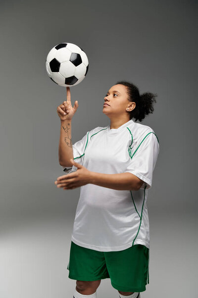 A female athlete wearing a white jersey and green shorts spins a soccer ball on her fingertip.