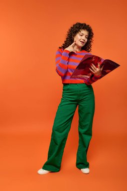 A young woman with curly hair poses in a vibrant outfit against a bright orange backdrop. clipart