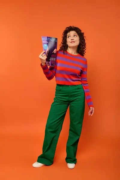 stock image A young woman with curly hair poses in vibrant attire against a bright orange background.