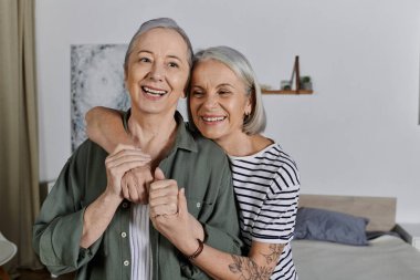 Olgun bir lezbiyen çift modern dairelerinde kucaklaşıyor. İkisi de mutlu bir şekilde gülümsüyor ve birbirlerine çok aşıklar..