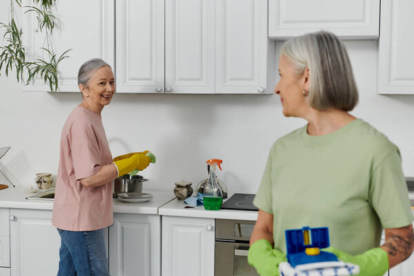 An older lesbian couple cleans their modern kitchen together, sharing a moment of intimacy and domestic bliss.