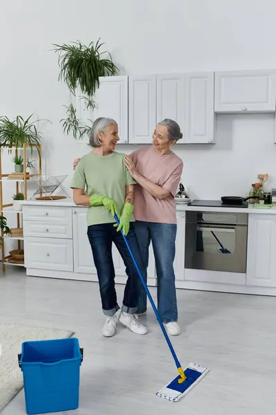 stock image A mature lesbian couple cleans their modern apartment together, laughing and enjoying each others company.