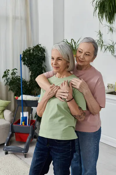 stock image A lesbian couple embraces in their modern apartment, with cleaning supplies nearby.