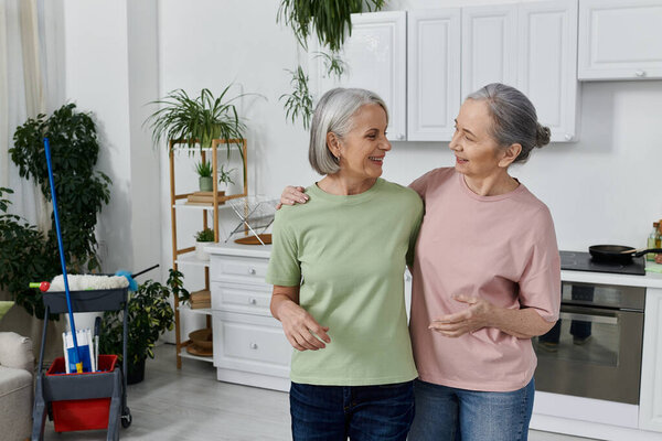 A mature lesbian couple cleans their modern apartment together.