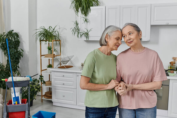 A mature lesbian couple enjoys a moment of tenderness while cleaning their modern apartment.