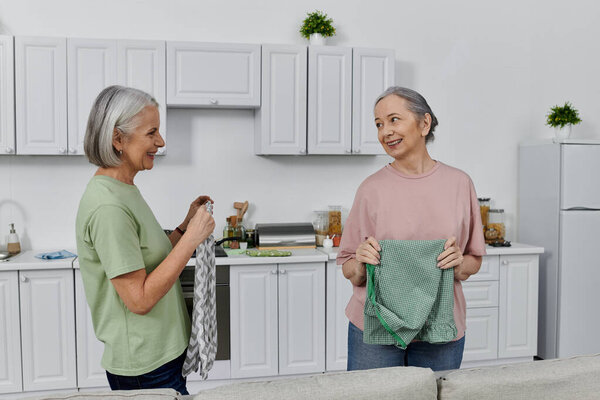 A lesbian couple cleans their modern apartment kitchen, sharing a lighthearted moment together.