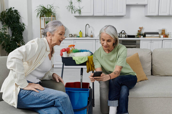 Взрослая лесбийская пара расслабляется на диване после уборки их современной квартиры вместе.