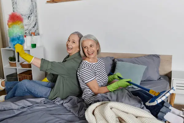 stock image Two mature lesbian women in casual attire are cleaning their modern apartment together, while smiling and having fun.