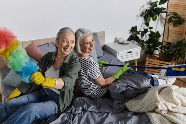 Two mature lesbian women are cleaning their modern apartment together. They are laughing and enjoying their time together.