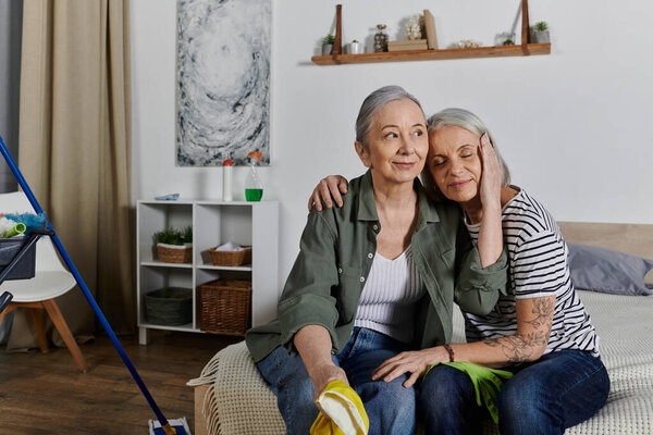 Lesbian couple resting on bed in modern apartment, showing affection as one woman rests head on others shoulder.