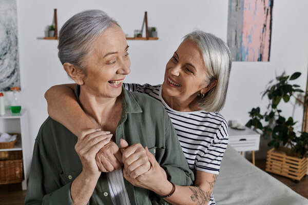 A mature lesbian couple embraces in a modern apartment, sharing a moment of love and laughter.