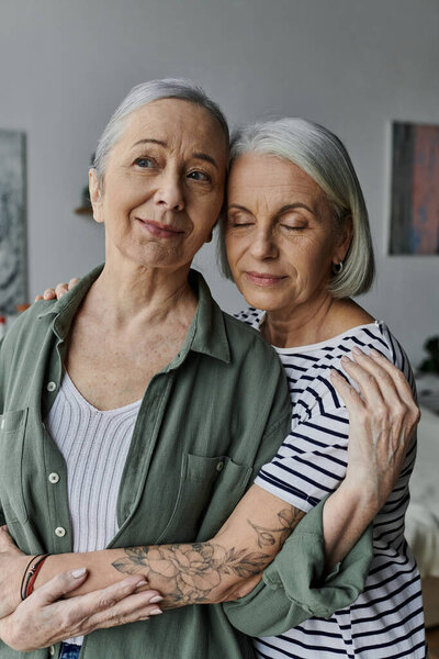 Two mature women embrace each other in a modern apartment setting, expressing their love and affection.