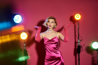 A woman in a pink satin dress poses under bright studio lights. clipart