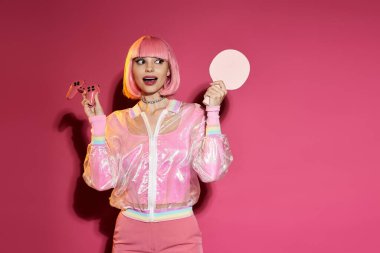Pembe elbiseli kadın pembe arka planda oyun kumandası ve pembe masa tenisi raketi tutuyor..