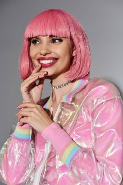 Pembe saçlı, gülümseyen bir kadın canlı bir holografik ceket giyer..