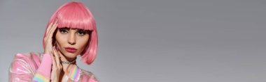 Parlak pembe saçlı ve pastel pembe ceketli bir kadın stüdyo ortamında fotoğraf için poz veriyor..