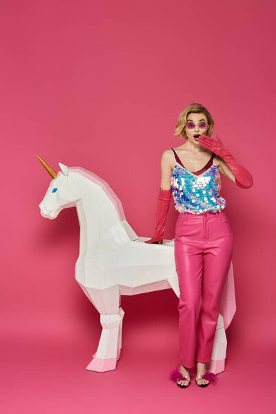 Женщина в яркой одежде стоит рядом с белым единорогом, удивлённая..