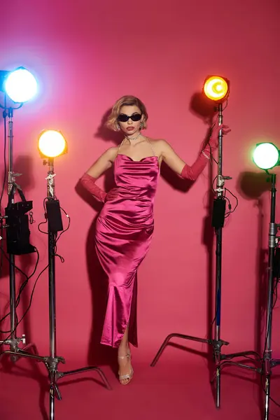 stock image A woman in a vibrant pink dress poses against a pink background, lit by studio lights.