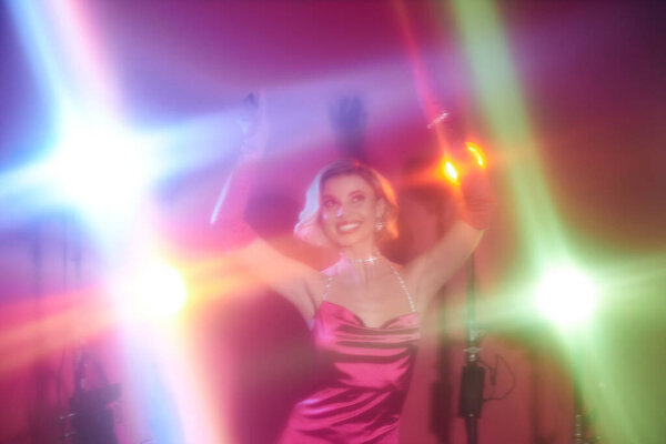 Женщина в розовом платье танцует под яркими огнями.