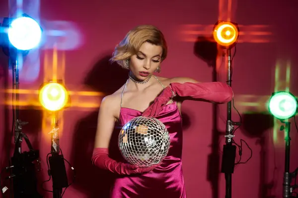stock image A glamorous woman in a vibrant pink dress holds a disco ball under colorful lights.
