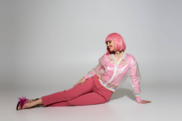 A woman with pink hair and a transparent jacket poses on a white background.