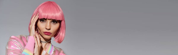 A woman with bright pink hair and a pastel pink jacket poses for a photo in a studio setting.