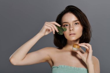 A woman uses a jade roller on her face, holding a small jar of cream in her other hand. clipart