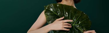 A woman poses with a large, wet leaf against a dark green backdrop. clipart