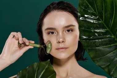 Bir kadın, yeşil yapraklardan oluşan bir zemin üzerinde yeşim bir silindir kullanıyor..