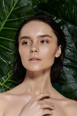 Islak saçlı güzel bir kadın canlı yeşil yaprakların arkasında poz verir..