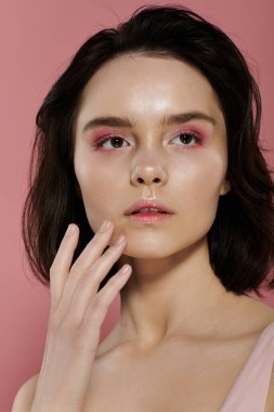 Pembe göz farı olan bir kadın canlı pembe bir arka plana karşı poz verir..
