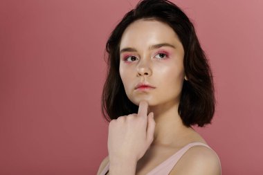 Pembe göz farı olan bir kadın canlı pembe bir arka plana karşı poz verir..