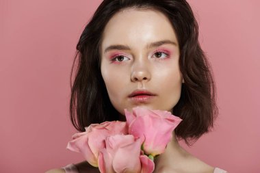 Pembe göz farı olan bir kadın pembe bir gül buketini katı pembe arka planda tutar..