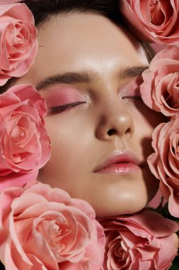 Close-up of a woman with her eyes closed surrounded by pink roses. clipart