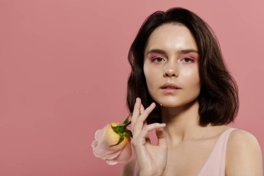 Pembe göz farı olan bir kadın pembe bir gül tutan, yumuşak pembe bir arka plana karşı poz verir..