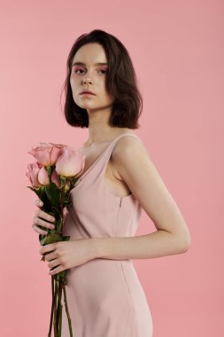 Pembe elbiseli siyah saçlı kadın pembe arka planda güller tutuyor..
