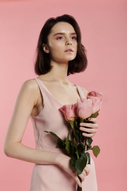 Pembe elbiseli bir kadın pembe arka planda pembe güller tutuyor..