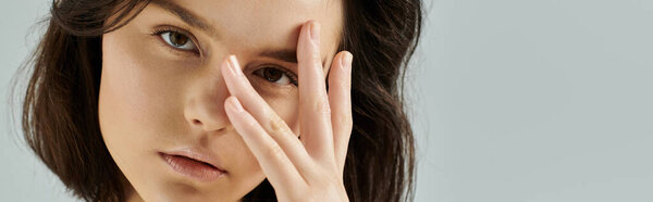 Крупный план портрета женщины с темными волосами, закрывающей один глаз рукой, выглядящей загадочно.