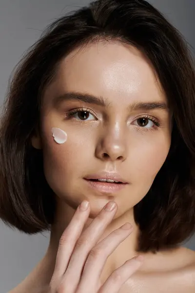 stock image A woman with short brown hair is applying cream to her cheek.