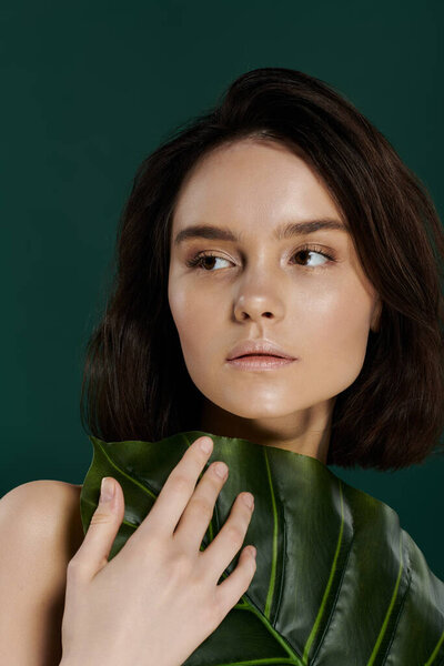 Красивая женщина позирует с большим зеленым листом на ярком зеленом фоне.