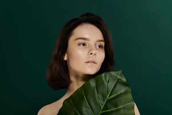 stock image A woman poses with a large, green leaf against a vibrant emerald backdrop.