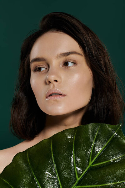 Красивая женщина позирует с большим зеленым листом на ярком фоне.