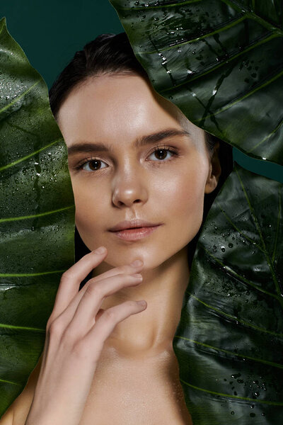 A close-up portrait of a beautiful woman posing with large green leaves.