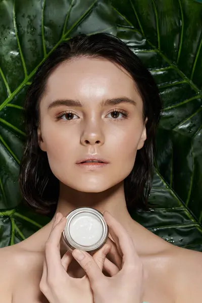 stock image A woman holds a jar of cream against a backdrop of vibrant green foliage.