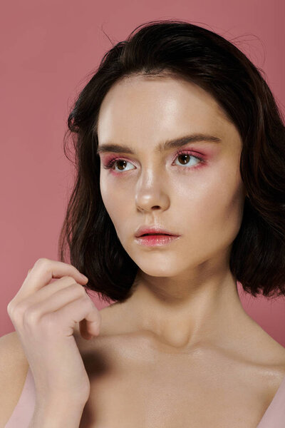 Женщина с короткими темными волосами на розовом фоне, мягко освещенная.